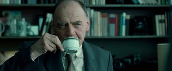 Movie still from “Unknown” (2011), directed by Jaume Collet-Serra – An older man in a suit and tie drinking a cup of coffee; Close Up shot, Low angle