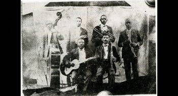 Movie still from “Uprooted: The Journey of Jazz Dance” (2020), directed by Khadifa Wong – An old photo of a group of men playing musical instruments; Extreme Close Up shot, Overhead angle
