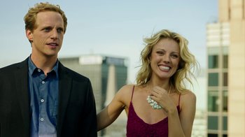 Movie still from “Urge” (2016), directed by Aaron Kaufman – A man and a woman standing next to each other in front of a building; Medium shot, Low angle