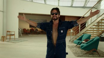 Movie still from “Urge” (2016), directed by Aaron Kaufman – A man with his arms outstretched in a room; Medium shot, Low angle