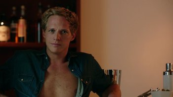 Movie still from “Urge” (2016), directed by Aaron Kaufman – A shirtless man with a drink in his hand; Close Up shot, High angle