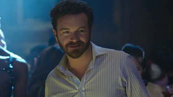 Movie still from “Urge” (2016), directed by Aaron Kaufman – A man in a striped shirt is smiling for the camera; Close Up shot, Over the shoulder angle