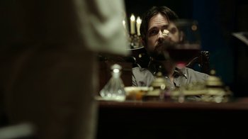 Movie still from “Urge” (2016), directed by Aaron Kaufman – A man sitting at a table with a glass of red wine in front of him; Medium shot, Over the shoulder angle