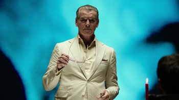 Movie still from “Urge” (2016), directed by Aaron Kaufman – A man in a white suit is smoking a cigarette; Close Up shot, Low angle