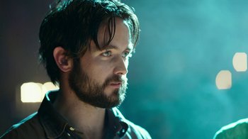 Movie still from “Urge” (2016), directed by Aaron Kaufman – A person with a beard; Close Up shot, Over the shoulder angle