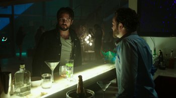 Movie still from “Urge” (2016), directed by Aaron Kaufman – Two men are sitting at a bar talking to each other; Medium shot, Over the shoulder angle