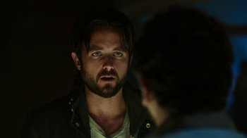 Movie still from “Urge” (2016), directed by Aaron Kaufman – A person looking at a mirror; Close Up shot, Over the shoulder angle