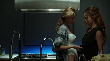 Movie still from “Urge” (2016), directed by Aaron Kaufman – Two women in a kitchen looking at something on a tablet; Medium shot, Over the shoulder angle