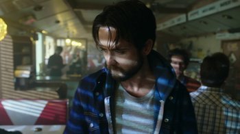 Movie still from “Urge” (2016), directed by Aaron Kaufman – A man with a beard and striped shirt looking at the camera; Close Up shot, Low angle