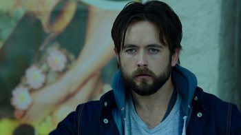 Movie still from “Urge” (2016), directed by Aaron Kaufman – A person with a beard; Close Up shot, Over the shoulder angle