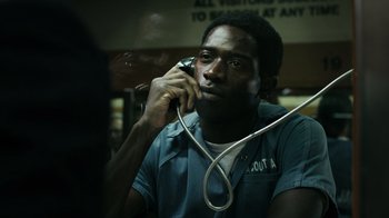Movie still from “Snowfall” (2017), directed by Hiro Murai – A man holding a phone to his ear while sitting in a room; Close Up shot, High angle