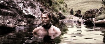 Movie still from “Valhalla Rising” (2009), directed by Nicolas Winding Refn – A man in a body of water wearing a black collar; Wide shot, High angle