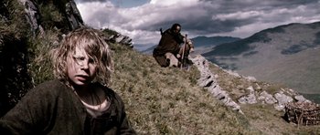 Movie still from “Valhalla Rising” (2009), directed by Nicolas Winding Refn – A man sitting on top of a hill next to a woman; Medium shot, Low angle