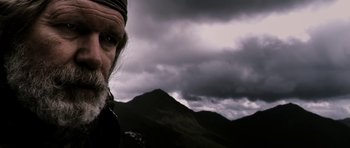 Movie still from “Valhalla Rising” (2009), directed by Nicolas Winding Refn – A man with a beard is standing in front of some mountains; Close Up shot, Low angle