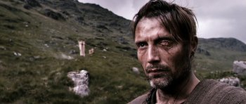 Movie still from “Valhalla Rising” (2009), directed by Nicolas Winding Refn – A person with a mountain in the background; Close Up shot, Over the shoulder angle