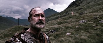Movie still from “Valhalla Rising” (2009), directed by Nicolas Winding Refn – A man with a beard and a mustache with a scar on his face; Medium shot, Low angle