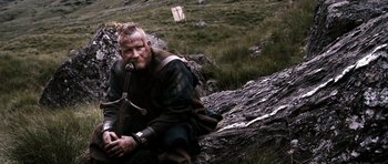 Movie still from “Valhalla Rising” (2009), directed by Nicolas Winding Refn – A man in a viking garb sitting on top of a tree stump; Medium shot, Low angle