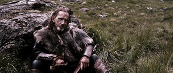 Movie still from “Valhalla Rising” (2009), directed by Nicolas Winding Refn – A man dressed as a viking sitting on the ground; Medium shot, Low angle