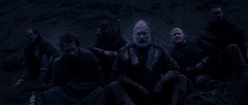 Movie still from “Valhalla Rising” (2009), directed by Nicolas Winding Refn – A group of men sitting on the ground in the dark; Medium shot, Low angle