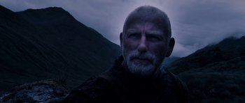 Movie still from “Valhalla Rising” (2009), directed by Nicolas Winding Refn – A person with a mountain in the background; Close Up shot, Low angle
