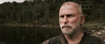 Movie still from “Valhalla Rising” (2009), directed by Nicolas Winding Refn – An older man with a beard is standing by the water; Close Up shot, Low angle