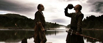 Movie still from “Valhalla Rising” (2009), directed by Nicolas Winding Refn – Two men in medieval garb standing next to a body of water; Medium shot, Over the shoulder angle