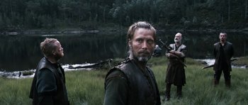 Movie still from “Valhalla Rising” (2009), directed by Nicolas Winding Refn – A man standing next to another man near a body of water; Medium shot, Over the shoulder angle