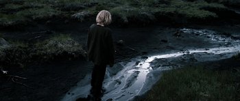 Movie still from “Valhalla Rising” (2009), directed by Nicolas Winding Refn – A person standing in a muddy area near a stream; Medium shot, High angle