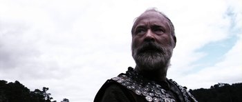 Movie still from “Valhalla Rising” (2009), directed by Nicolas Winding Refn – A man with a beard wearing a chain mail shirt; Close Up shot, Low angle