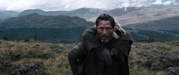 Movie still from “Valhalla Rising” (2009), directed by Nicolas Winding Refn – A man with long hair and beard standing in a field; Medium shot, Over the shoulder angle