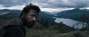 Movie still from “Valhalla Rising” (2009), directed by Nicolas Winding Refn – A man with long hair and a goatee stares into the distance; Wide shot, Low angle