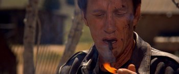 Movie still from “Vampires” (1998), directed by John Carpenter – A man is smoking a cigarette while holding a fire; Close Up shot, Low angle