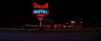 Movie still from “Vampires” (1998), directed by John Carpenter – A motel sign lit up at night with a person standing in front of it; Extreme Wide shot, Low angle