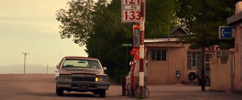 Movie still from “Vampires” (1998), directed by John Carpenter – A car parked on the side of the road next to a gas station; Wide shot, Low angle
