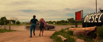 Movie still from “Vampires” (1998), directed by John Carpenter – A man and a woman running down a dirt road near a car; Wide shot, Over the shoulder angle