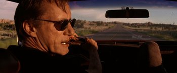 Movie still from “Vampires” (1998), directed by John Carpenter – A man in sunglasses is smoking a cigar while sitting in the drivers seat of a car; Close Up shot, Low angle