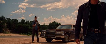 Movie still from “Vampires” (1998), directed by John Carpenter – A man standing in front of a car on a dirt road; Wide shot, Low angle