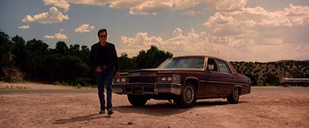 Movie still from “Vampires” (1998), directed by John Carpenter – A man standing in front of a car on a dirt road; Wide shot, Low angle