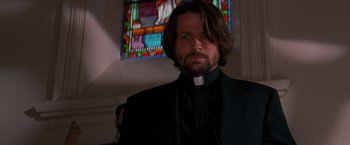 Movie still from “Vampires” (1998), directed by John Carpenter – A man wearing a priest's outfit in front of a stained glass window; Close Up shot, Low angle