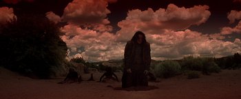 Movie still from “Vampires” (1998), directed by John Carpenter – A man standing in the sand under a cloudy sky; Wide shot, Low angle