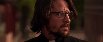 Movie still from “Vampires” (1998), directed by John Carpenter – A man with a beard wearing glasses and a priest's outfit; Close Up shot, Low angle