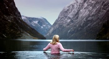 Movie still from “Violent” (2014), directed by Andrew Huculiak – A woman sitting on a surfboard in a body of water; Wide shot, High angle