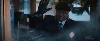 Movie still from “Violent Night” (2022), directed by Tommy Wirkola – A man wearing a hat and gloves waving; Close Up shot, Over the shoulder angle