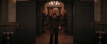 Movie still from “Violent Night” (2022), directed by Tommy Wirkola – A woman talking on a cell phone while standing in front of a group of men; Medium shot, Low angle