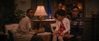 Movie still from “Violent Night” (2022), directed by Tommy Wirkola – A woman and a girl sitting on a couch in front of a lamp; Medium shot, Over the shoulder angle