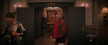 Movie still from “Violent Night” (2022), directed by Tommy Wirkola – A young man standing in a room with a red shirt on; Medium shot, Over the shoulder angle