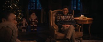 Movie still from “Violent Night” (2022), directed by Tommy Wirkola – A man sitting in a chair in front of a santa clause statue; Medium shot, Over the shoulder angle
