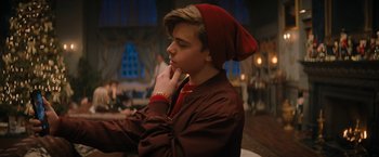 Movie still from “Violent Night” (2022), directed by Tommy Wirkola – A young man wearing a red hat and a brown jacket; Medium shot, Over the shoulder angle