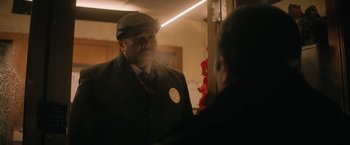 Movie still from “Violent Night” (2022), directed by Tommy Wirkola – A man wearing a hat and a suit talking to another man in a suit; Medium shot, Over the shoulder angle