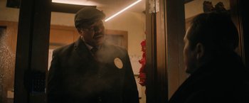 Movie still from “Violent Night” (2022), directed by Tommy Wirkola – A man in a suit and hat standing next to a door; Close Up shot, Low angle